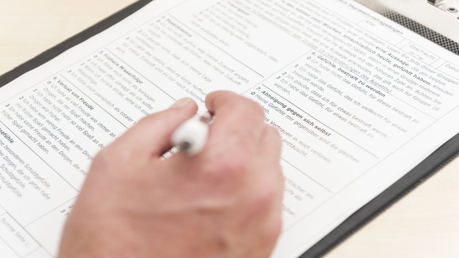 Eine Person füllt einen Aufnahmebogen mit verschiedenen Fragen zur psychischen Verfassung des Befragten aus.