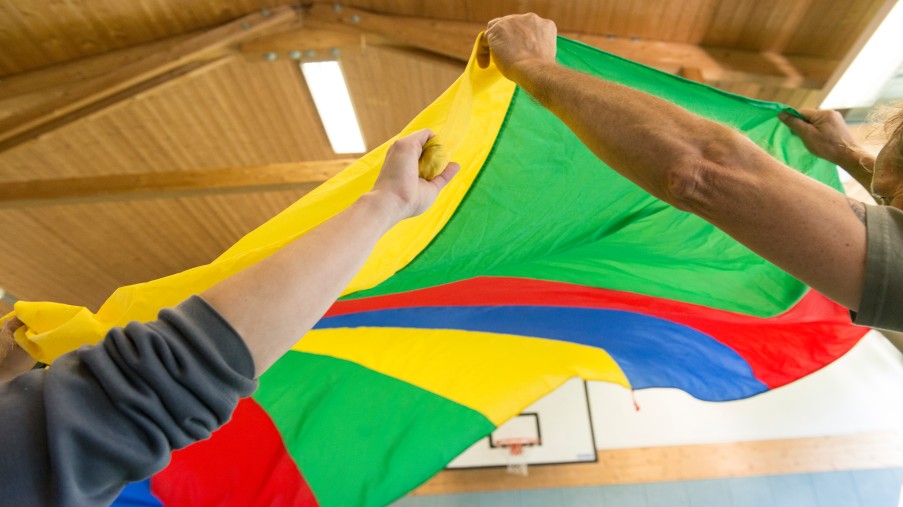 Zwei Personen reißen ein buntes Schwungtuch in die Höhe.