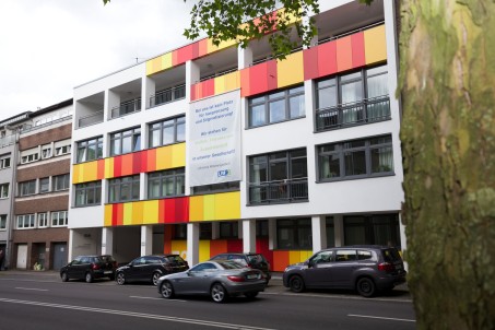Hausfassade mit roten, gelben und orangefarbenen Paneelen und einem Banner, das sich gegen Ausgrenzung und Stigmatisierung auspricht und für Tolreanz wirbt
