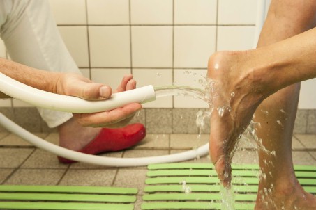 Einer Frau werden die Füße mit einem Wasserschlauch abgespritzt